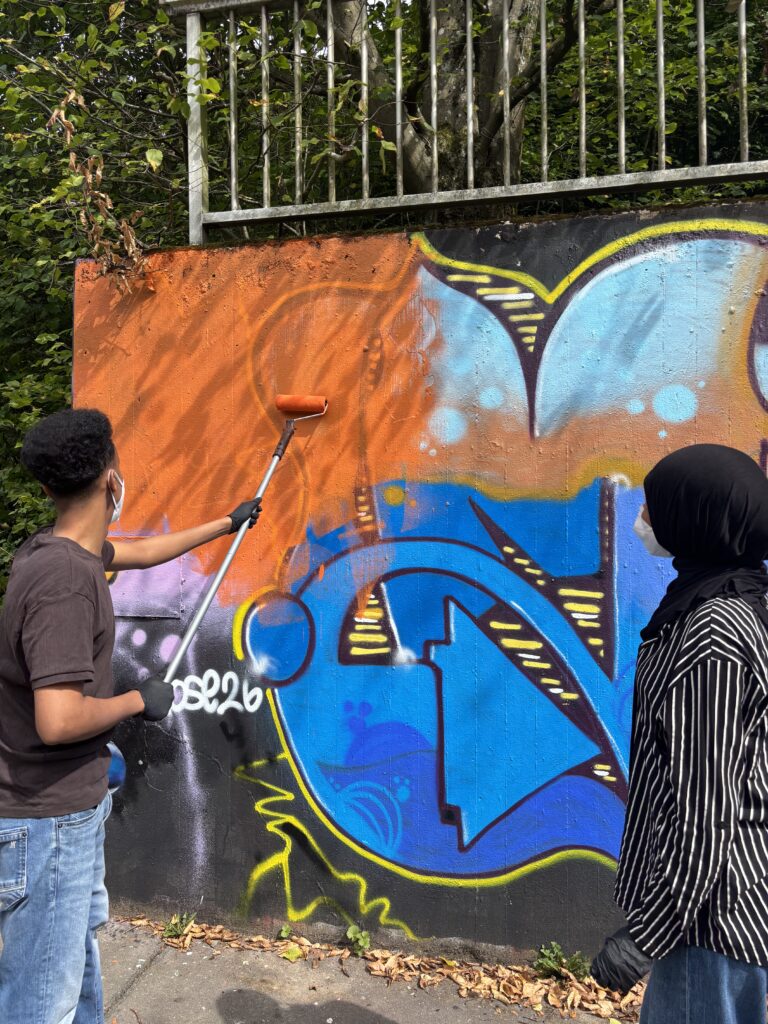 Junger Mann überstreicht ein Graffiti mit oranger Farbe